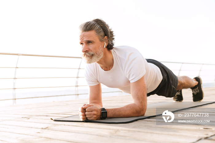 Image of concentrated mature man using earpod while doing exercise