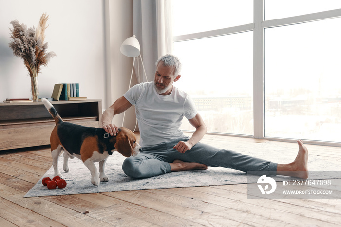 Happy senior man in sport clothing exercising at home near his dog