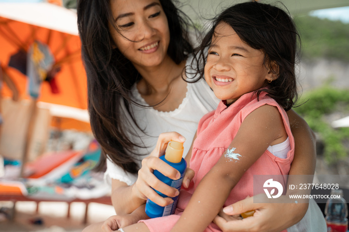 a daughter feels amused when mother give a sunblock to his arm