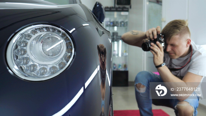 A young professional photographer (a guy, a man) takes pictures of a car in a car salon. Concept: lifestyle, new photo, car, photo apron, flash, exhibition.