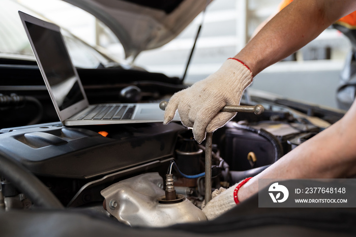 Hands of male mechanic worker maintaining car engine under hood of car at the repair garage. Male car mechanic working using wrench tool for examining, repair and maintenance at car service shop