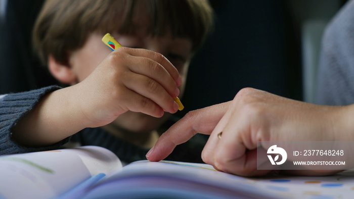 Child doing homework closeup face. Mother hand pointing at drawing figure on paper. Parent helping little boy with homeschooling