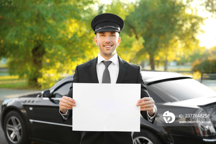 Young chauffeur standing with white board near luxury car on the street