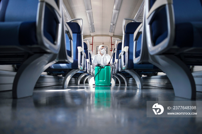 Public transportation healthcare. Man in white protection suit disinfecting and sanitizing subway train interior to stop spreading highly contagious coronavirus or COVID-19.