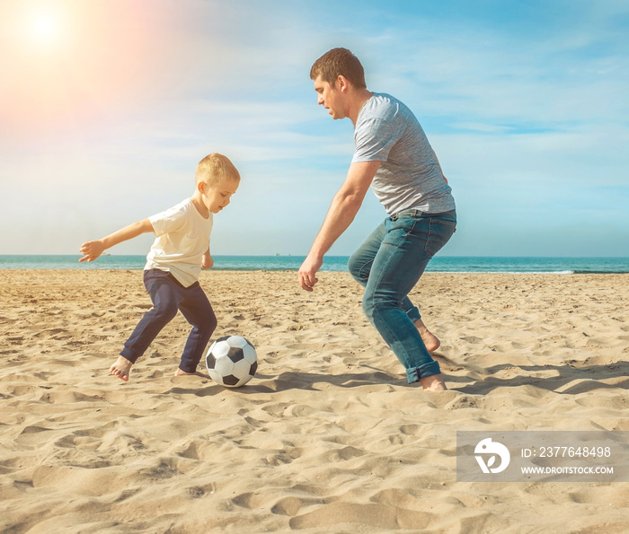 Father and son playing in football on sea coastline beach under