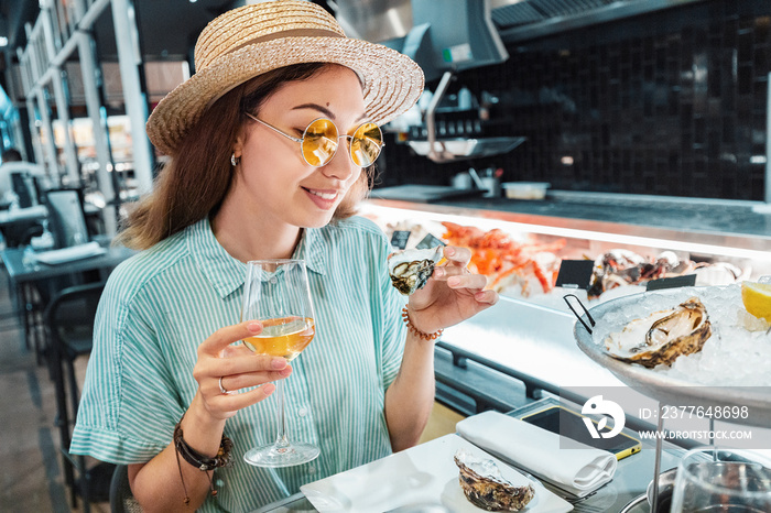 Asian woman tasting fresh raw oyster shellfish and drinking wine in seafood restaurant