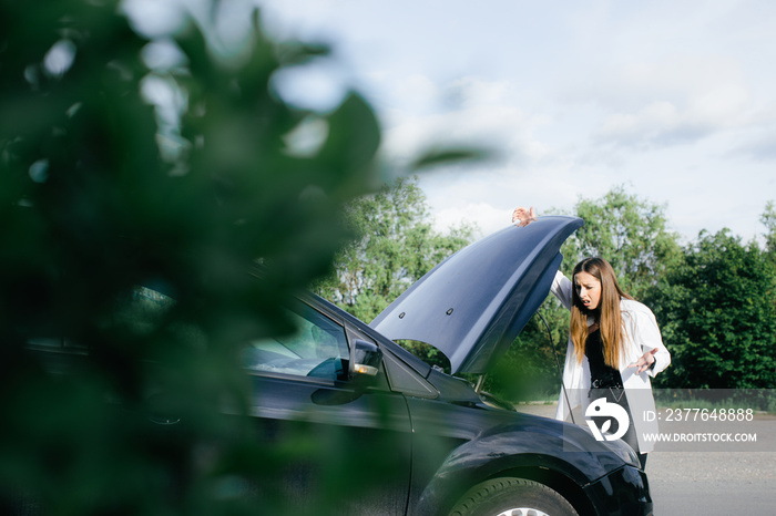 Frustrated young woman looking at broken down car engine on street