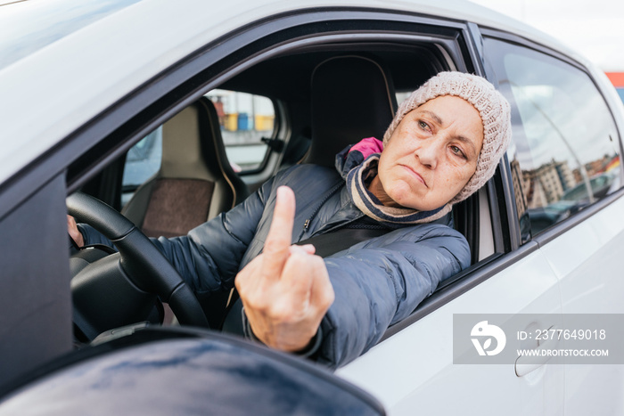 angry old lady driving a car and Showing middle finger doing fuck you bad expression , provocation and rude attitude.