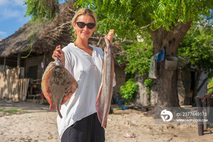 Young beautiful woman on holding fresh caught sea fish and small stingrays in her arms at a local food market on the island of Zanzibar, Tanzania, Africa