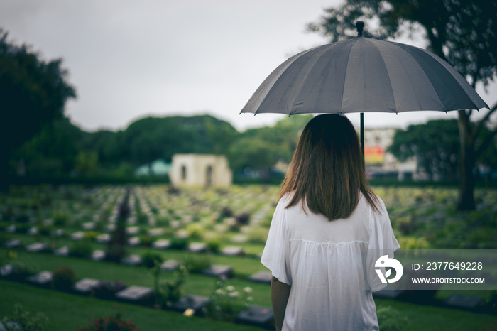 Young woman holding black umbrella mourning at cemetery