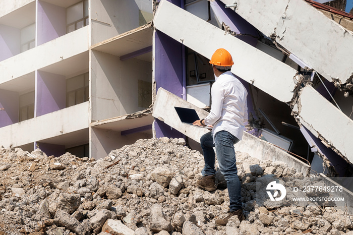 Engineer holding laptop is checking for destruction, demolishing building.