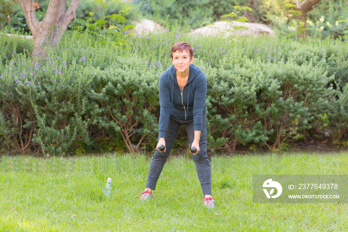 Happy smiling beautiful elderly woman doing sport exercises with dumbbells in a park on a sunny day.Fitness, sport, healthy, active retirement  and people concept.