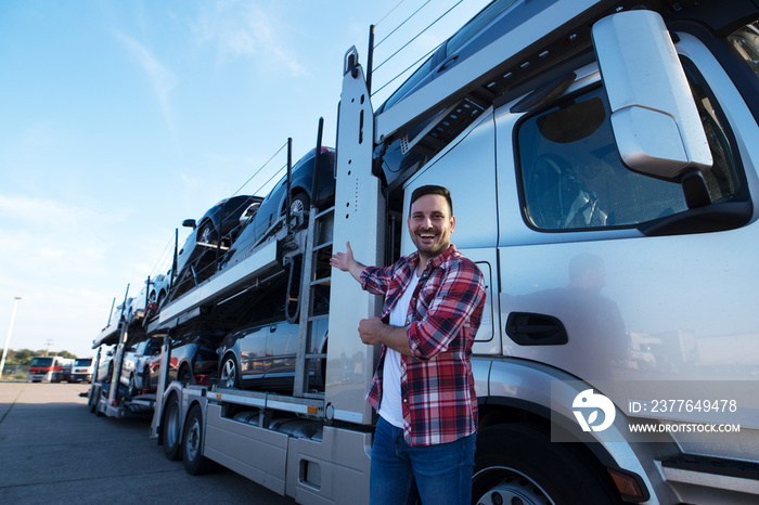 Middle aged trucker in front of truck trailer with cars. Transporting cars to the market.