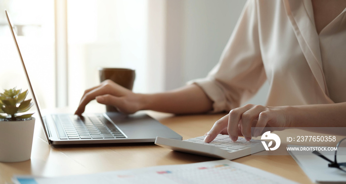 Close up Business woman using calculator and laptop for do math finance on wooden desk in office and business working background, tax, accounting, statistics and analytic research concept