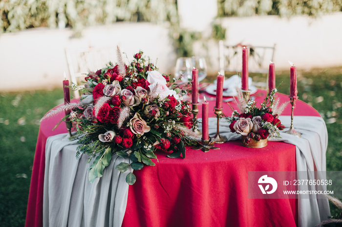 Wedding. Banquet. Grain. Artwork. At the banquet table with tablecloth colors Marsala, is the composition of flowers and greenery, cutlery and candles