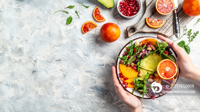 Girl holding vegan, detox Buddha bowl with avocado, persimmon, blood orange, nuts, spinach, arugula and pomegranate, balanced food. space for text. top view