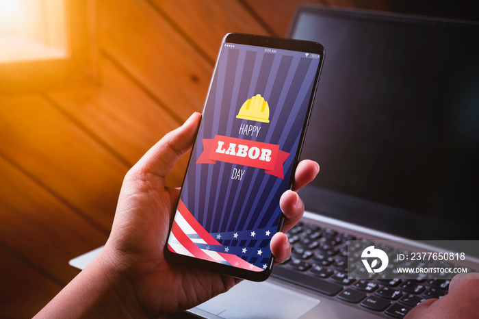 Happy labdor day mockup mobile phone concept. Close up business woman hand holding smart phone with Happy Labor Day on screen with blurred laptop background.