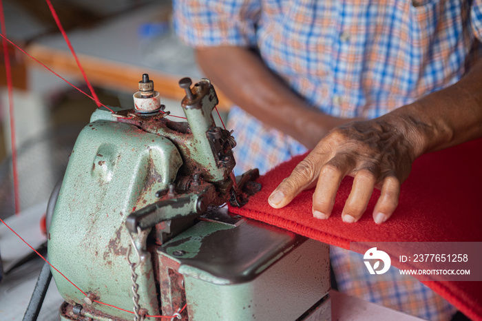 Close up hand of old man sewing a red rug