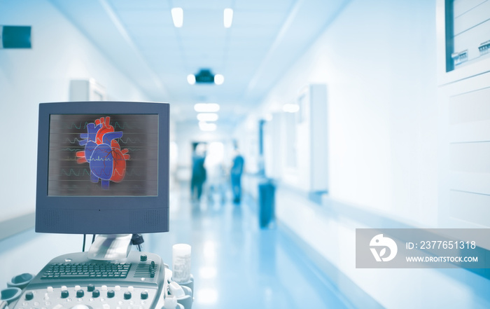 Ultrasonography equipment with heart image on the screen in the ER hallway with working doctors. Concept of an emergency care in a hospital with heart disease