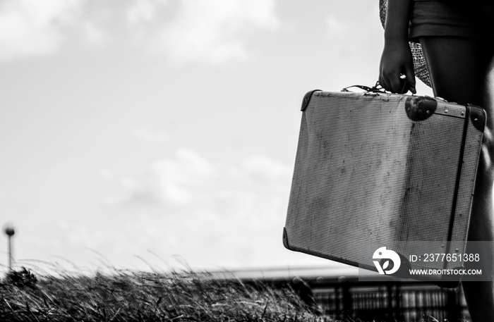 Ethnical girl standing with her old suitcase on the countryside