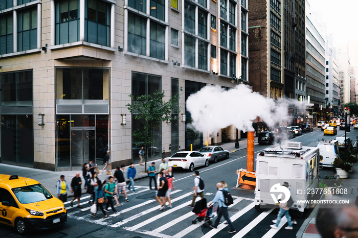 Pedestrians passing road on crosswalk in busy district of New York city while cars and taxi passing by, tall modern constructed buildings in crowded midtown and traffic of broadway city landmark