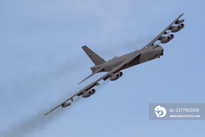 B52 Bomber turns towards the camera on a sunny day, the eight engined bomber leaving black smoke trails on a blue sky