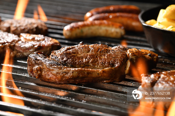 Cooked juicy steak meat beef with seasoning on a flaming grill surrounded by other meat and sausages.