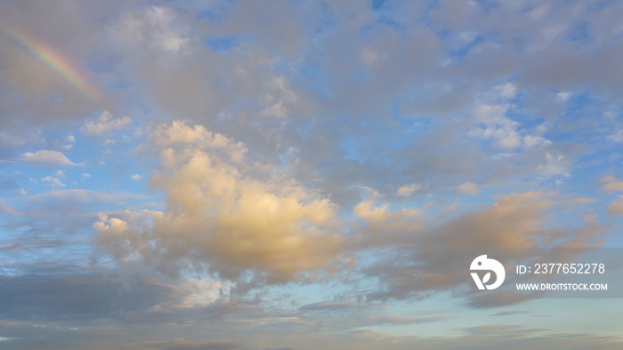 Late afternoon storm clouds break up revealing blue sky, white clouds and partial rainbow.