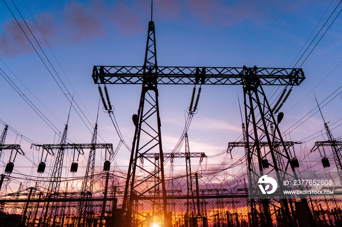 A silhouette of high voltage power lines against a colorful sky at sunrise.