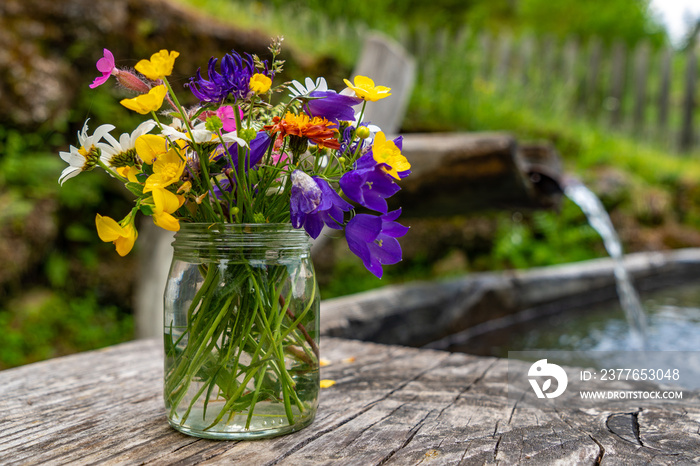 Blumen und Wildkräuter in einem Einmachglas an einem Brunnen