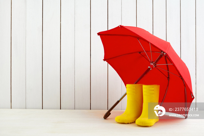 A pair of yellow rain boots and a umbrella on white wooden background