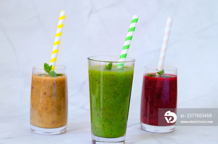 Top view of three different fresh delicious smoothies in a glasses made of peach, banana and berries with mint. Creative concept of healthy detox drink, diet or vegetarian food concept. Copy space.
