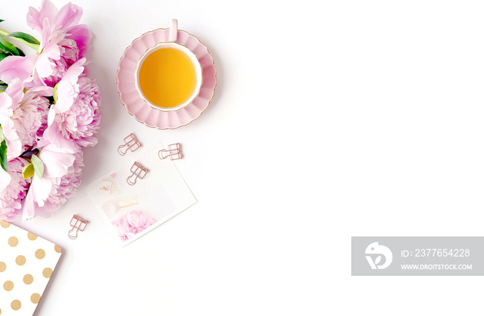 Styled flatlay with pink peonies, notebook and tea cup, copy space, white background