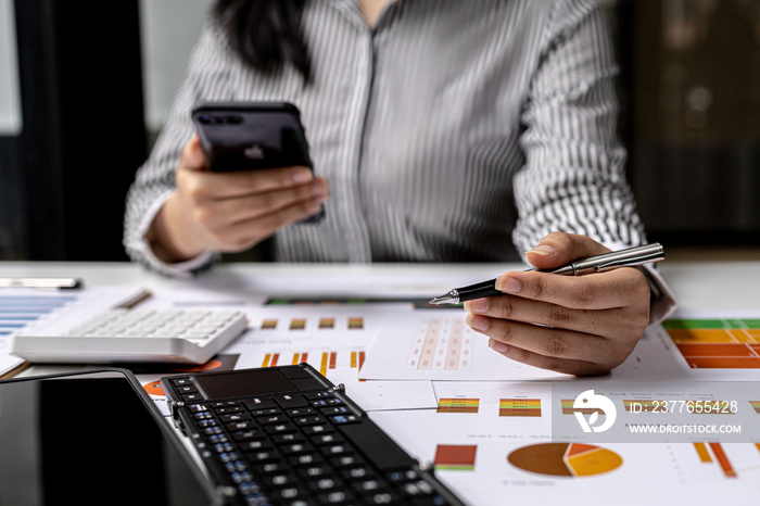 Person holding a mobile phone and pointing a pen at the document, the finance staff is reviewing the information of the company’s financial documents to conclude a meeting with the management.