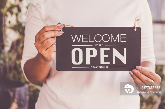 woman holding sign  welcome we’re open please come in  on cafe or restaurant.