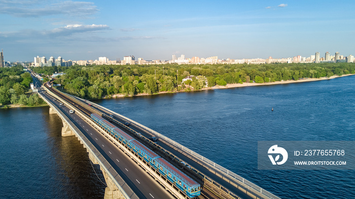 Aerial drone view of Metro railway bridge with train and Dnieper river from above, skyline of city of Kyiv, Kiev cityscape, Ukraine