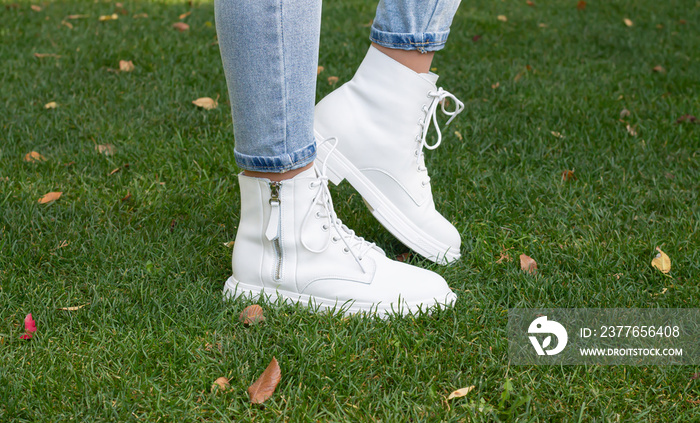 Woman legs in fashionable white casual boots on green grass background