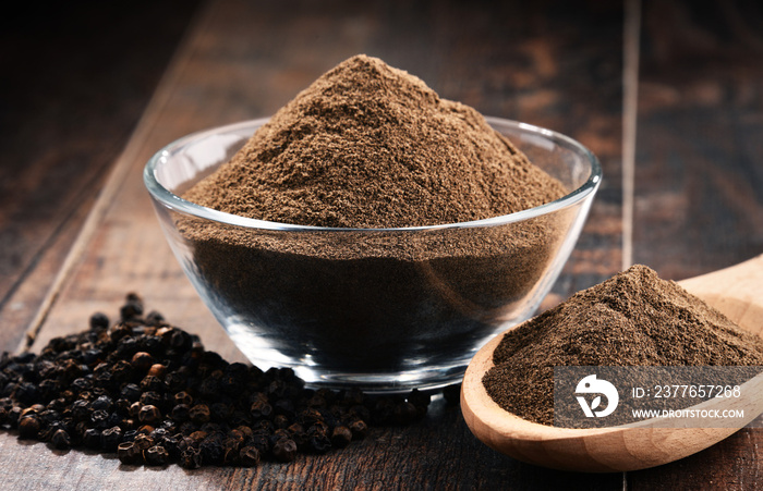 Composition with bowl of ground black pepper on wooden table