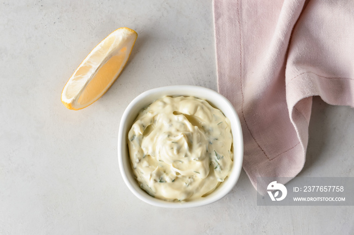 Bowl with tasty tartare sauce and lemon on light background, closeup