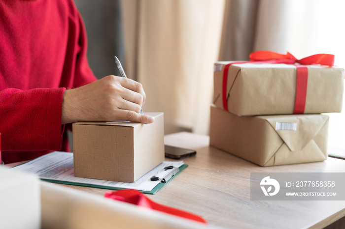 close-up of male hands filling out a mailing form on a parcel box in the office or at home. small business owner preparing to send christmas presents. postal delivery and people. shipment