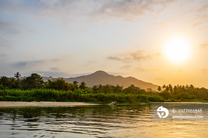 A wide river flows through the tropical rainforest of South America at a beautiful sunset where people bathe and enjoy life, Colombia Palomino