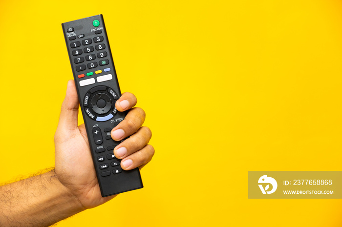 Close up male hand holding television remote control on isolated yellow background.