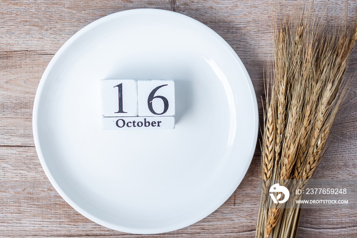 16 October calendar wooden with empty white plate and wheat on table background. Food Donation, Share, Volunteer and World Food day concept