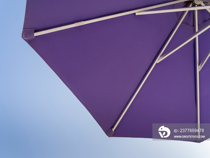 Purple beach umbrella. Blue sky in the background. View from below. Relaxing context. Summer holidays by the sea. General contest and location