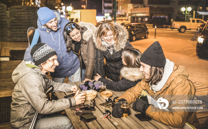 Happy friends drinking beer and eating chips at after ski bar - Friendship concept with cheerful people having fun at chalet restaurant resort with snow equipment - High iso image with focus on girls