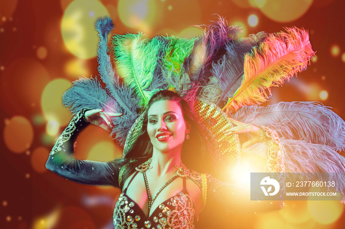 Beautiful young woman in carnival peacock costume. Beauty model woman at party over holiday background with magic glow. Christmas and New Year celebration. Glamour lady with perfect make up and