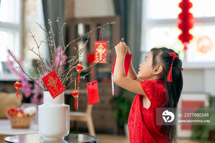 Cute little girl hanging handmade postcard containing new year greetings on branches