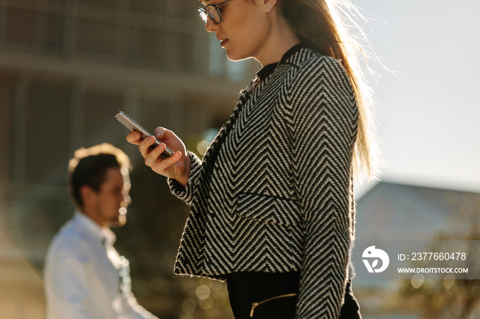 Businesswoman using mobile phone while walking on street to offi