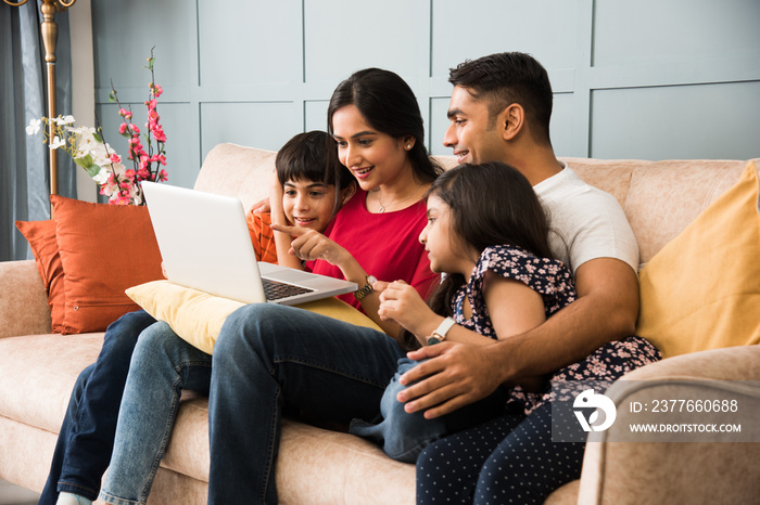 Indian family using smartphone, laptop or tablet, watching movie, surfing internet, sitting on sofa