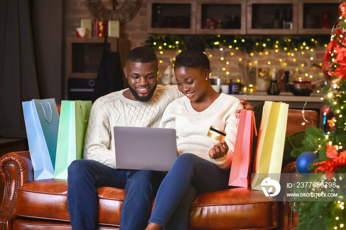 Afro couple buying gifts online, using laptop and credit card